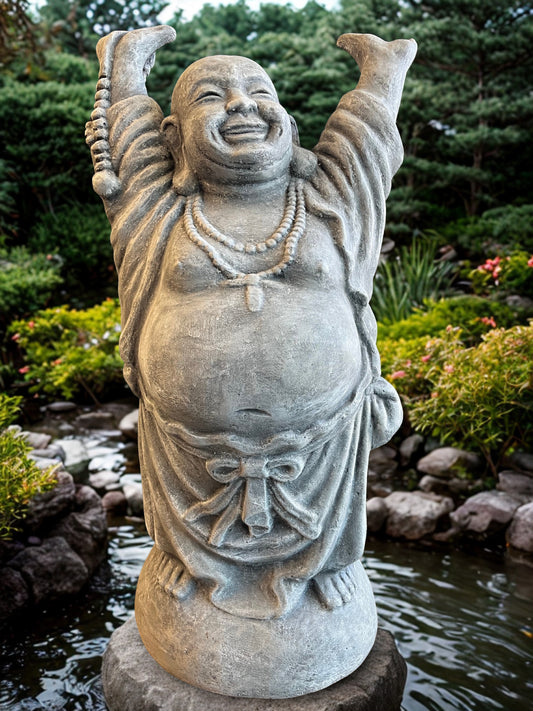 Stone statue of a laughing Buddha in a garden setting with water and plants.