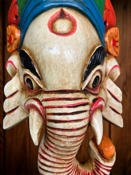 Decorative mask with Ganesh elephant head and colorful details on a wooden background