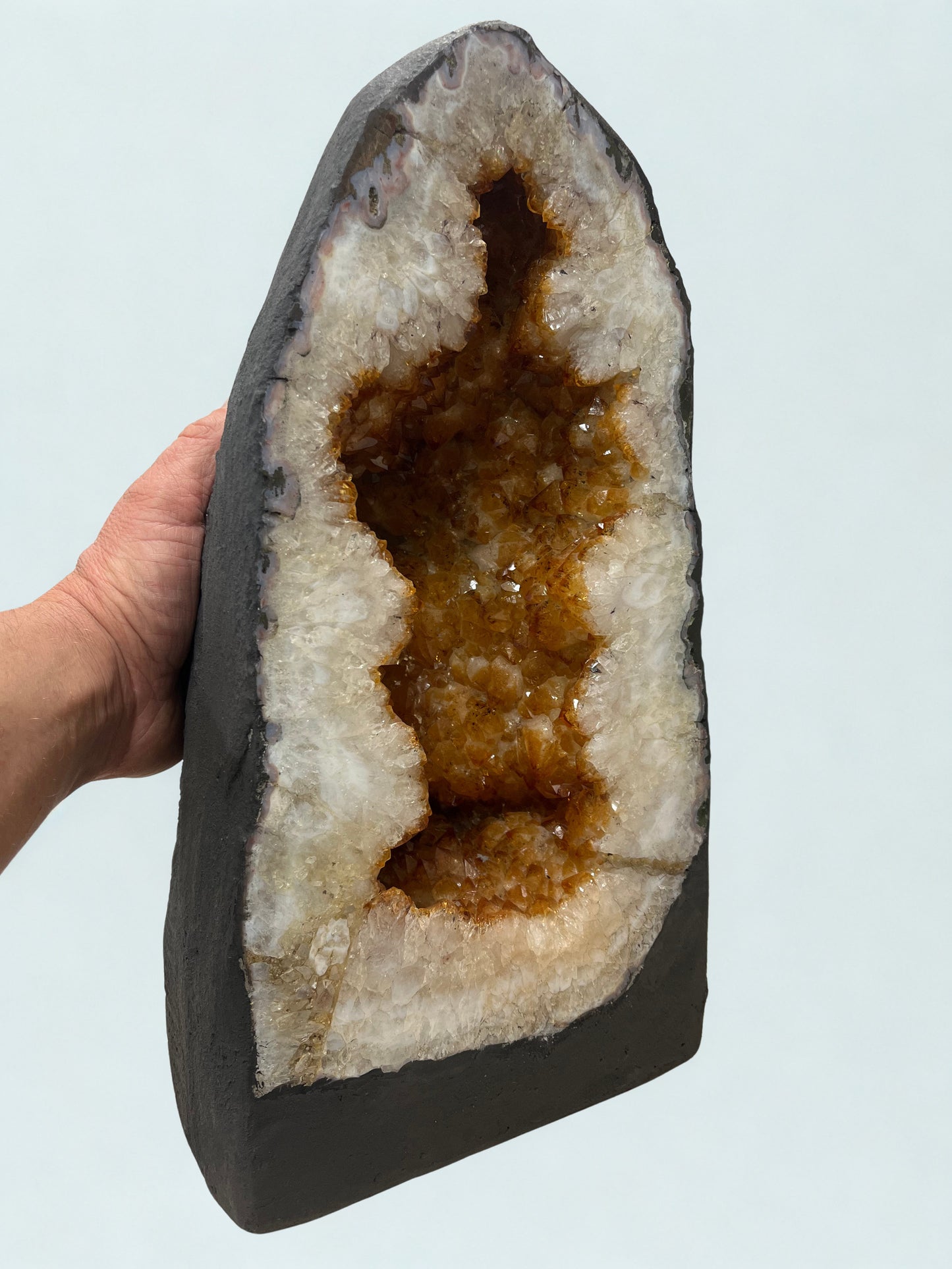Citrine Geode with brown interior held by a hand against a light blue background