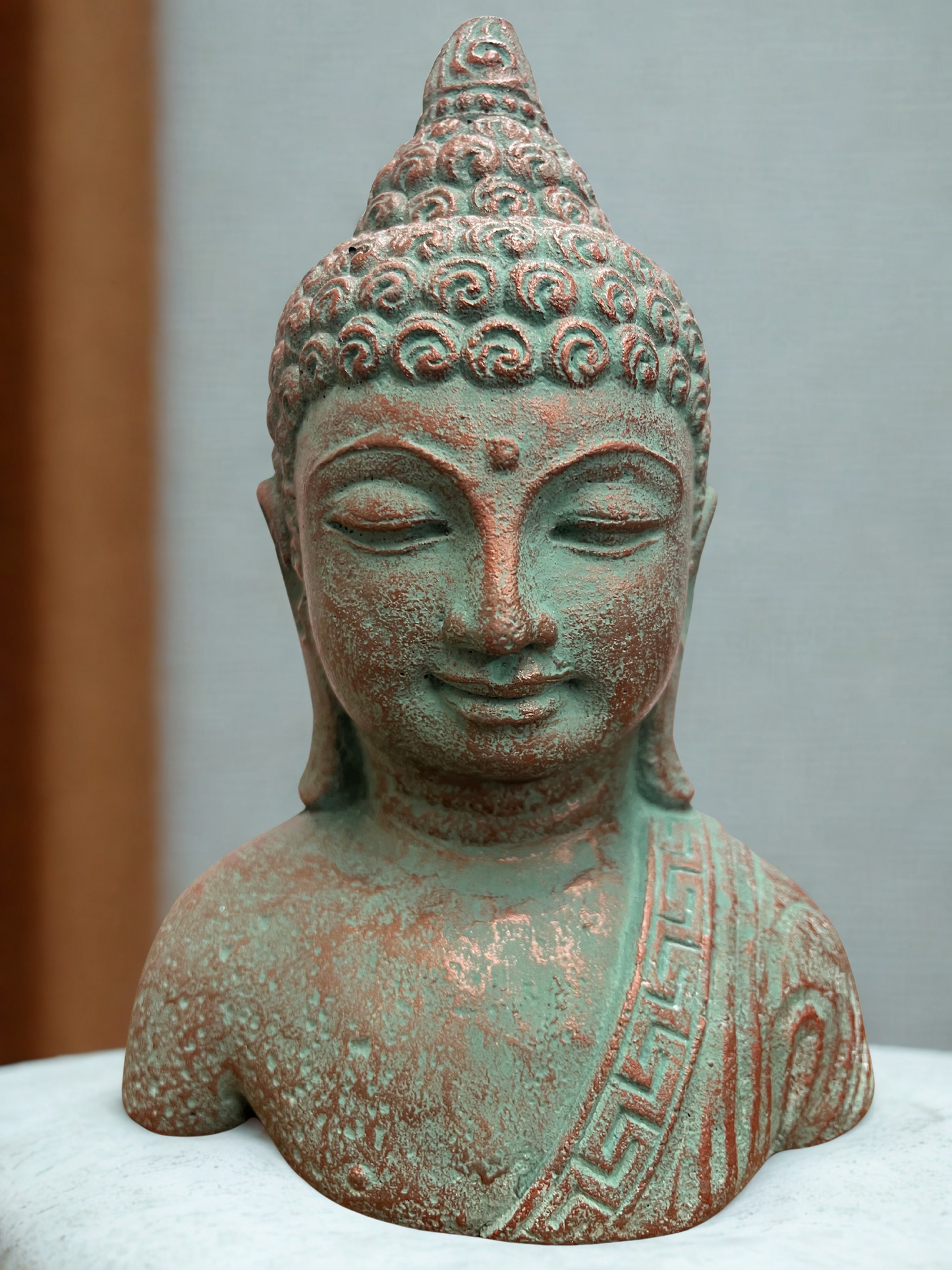 Bronze color statue of a Buddha head on a white surface with a neutral background
