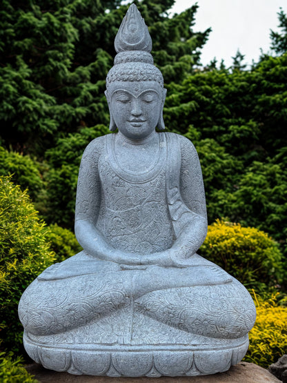 Stone statue of a seated Buddha in a garden setting with greenery.