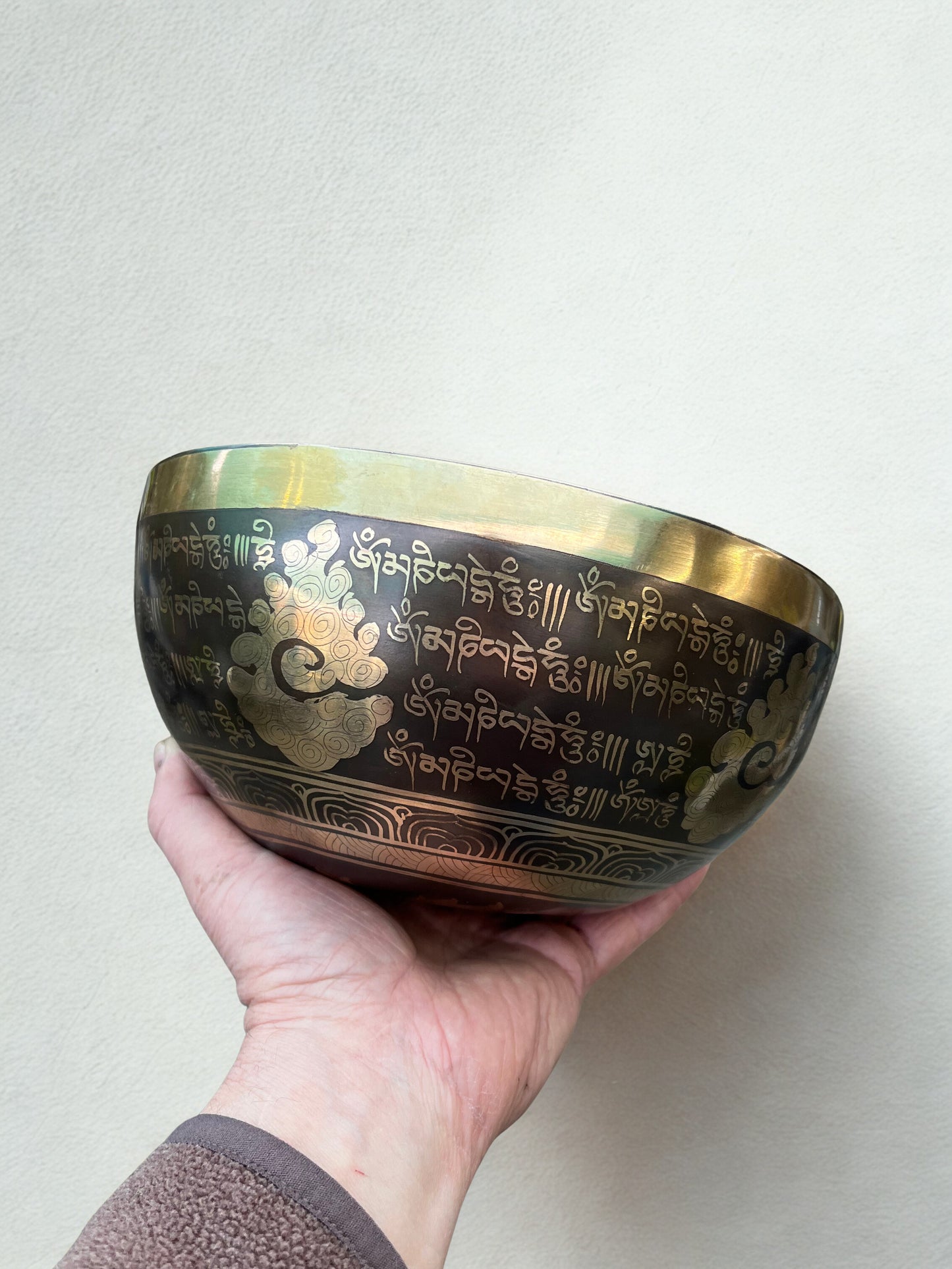 Hand holding a brass sound healing sound therapy singing bowl with engraved designs on a plain background