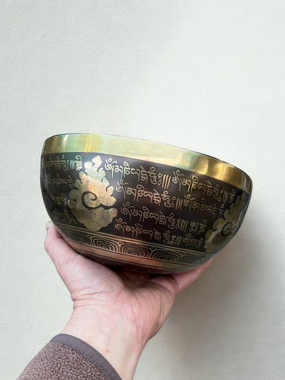 Hand holding a brass sound healing sound therapy singing bowl with engraved designs on a plain background