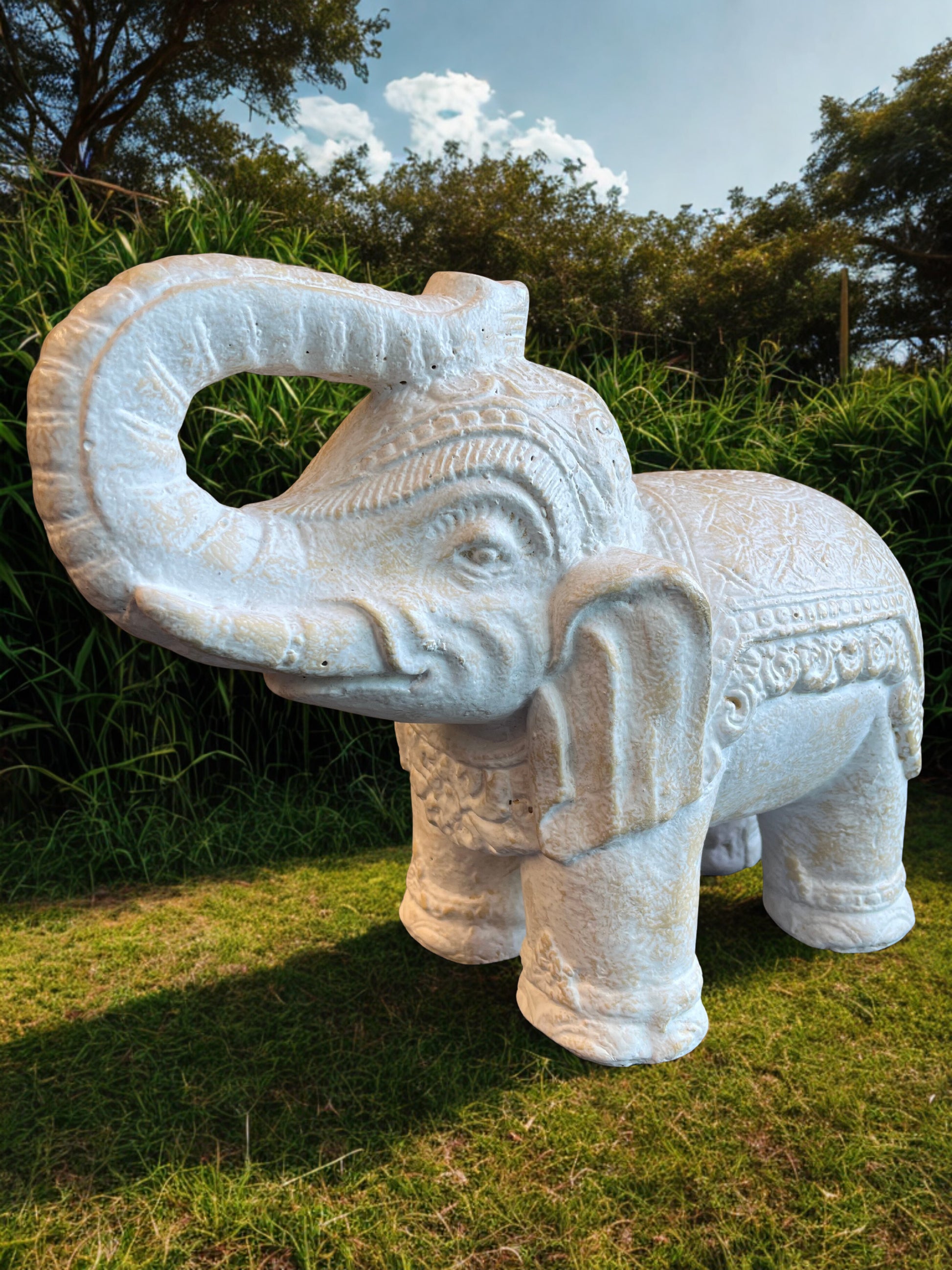 Decorative stone elephant statue in a natural setting with trees and grass.