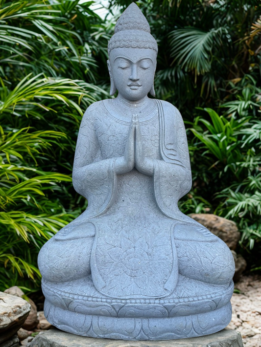 Stone Buddha statue in a meditative pose with greenery in the background