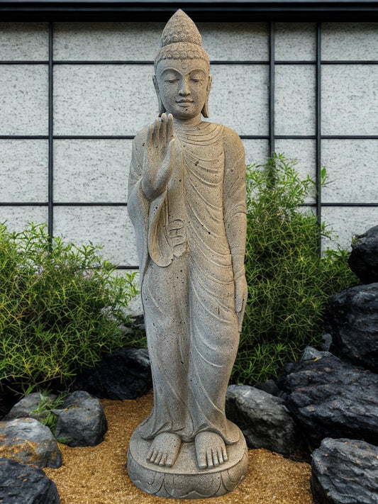Stone statue of a Buddha figure in a garden setting with rocks and plants.