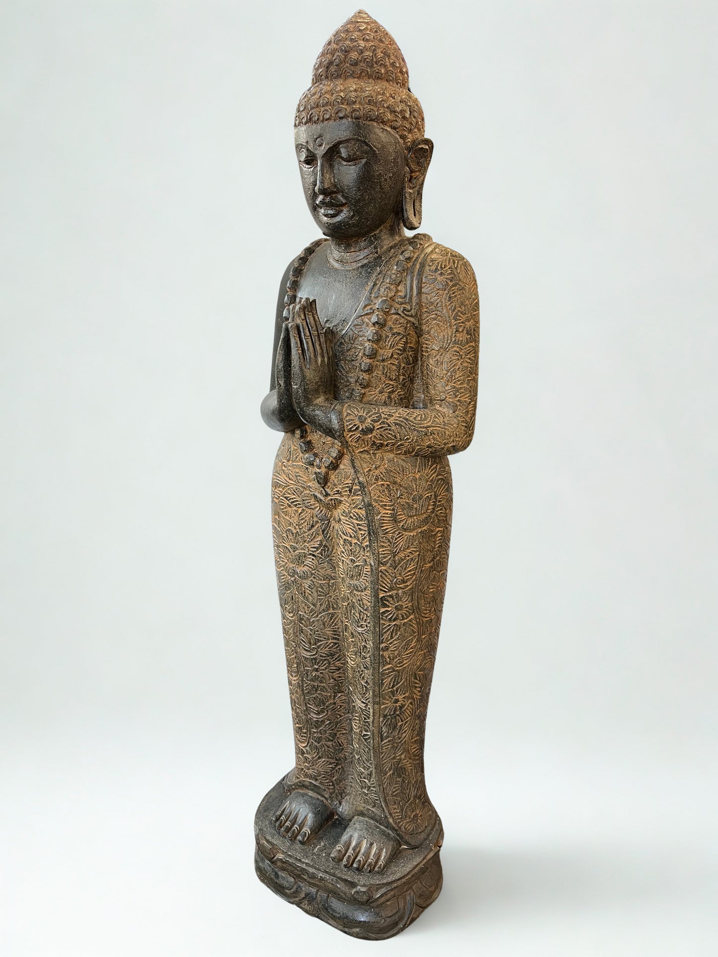 Statue of a standing meditating Buddha figure in namaste pose on a white background