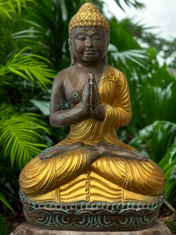 Statue of a meditating Buddha with gold and bronze colors against a green leafy background