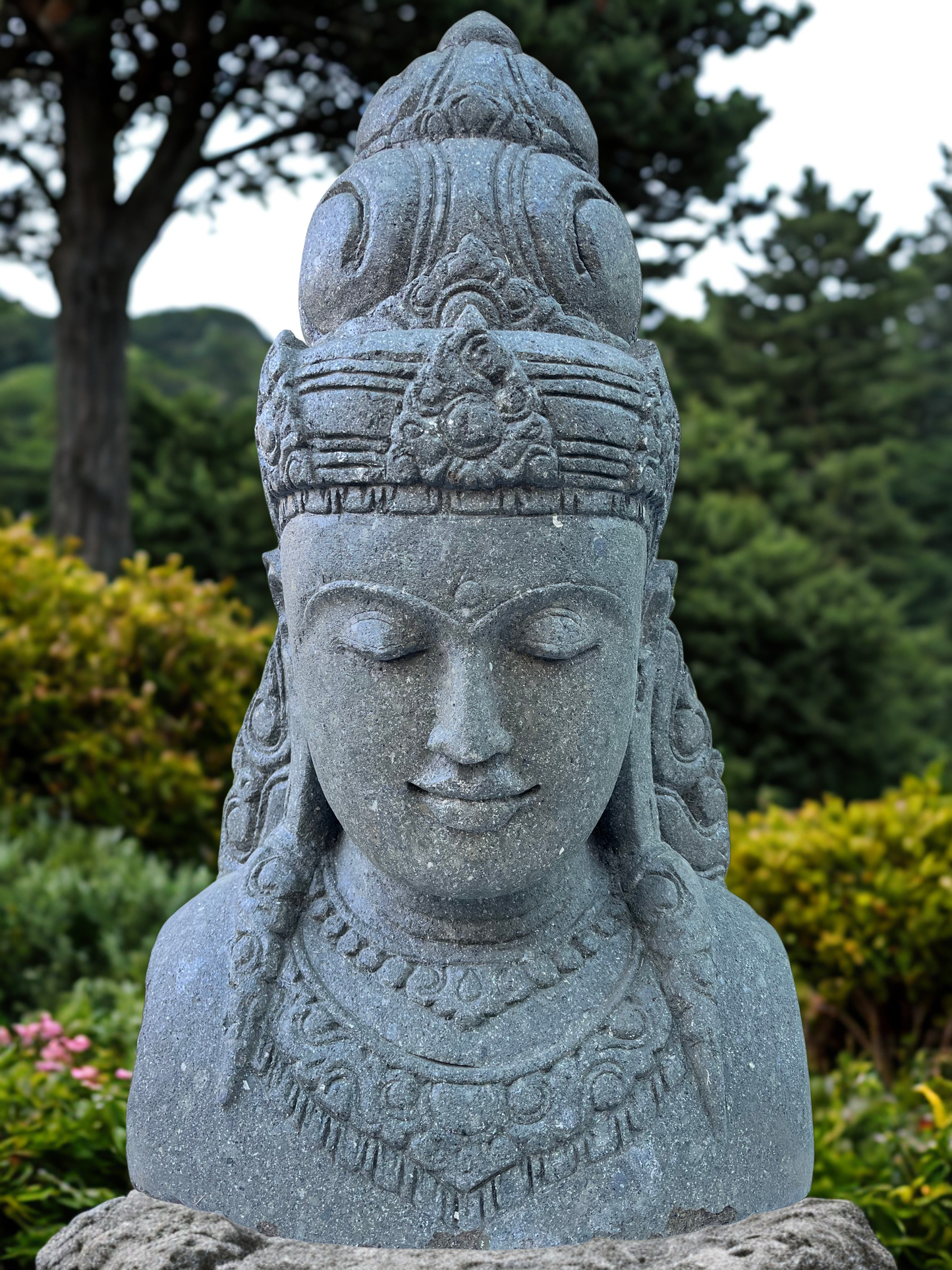 Stone statue of a goddess deity sculpture with intricate details in a garden setting