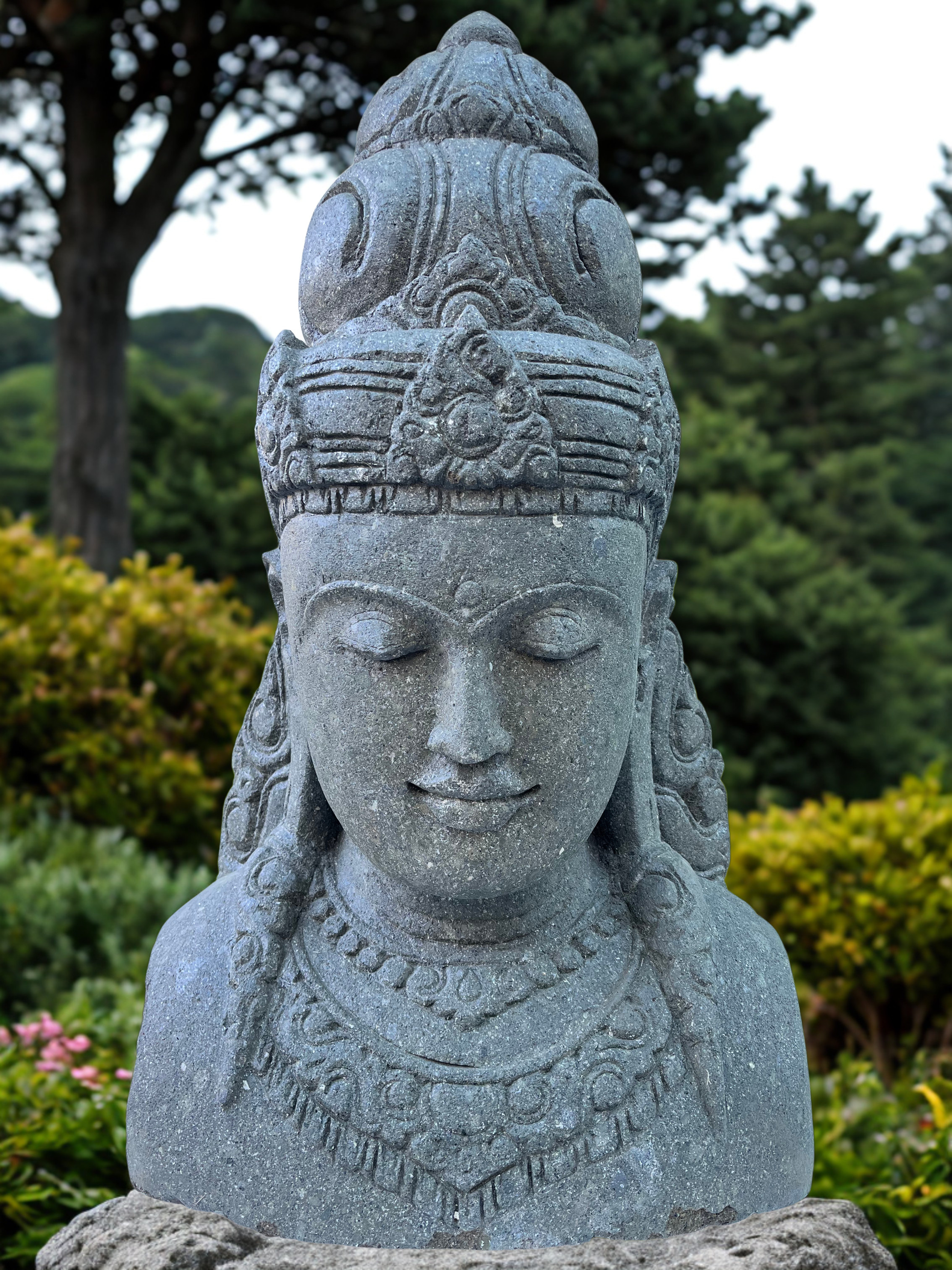 Stone statue of a goddess deity sculpture with intricate details in a garden setting