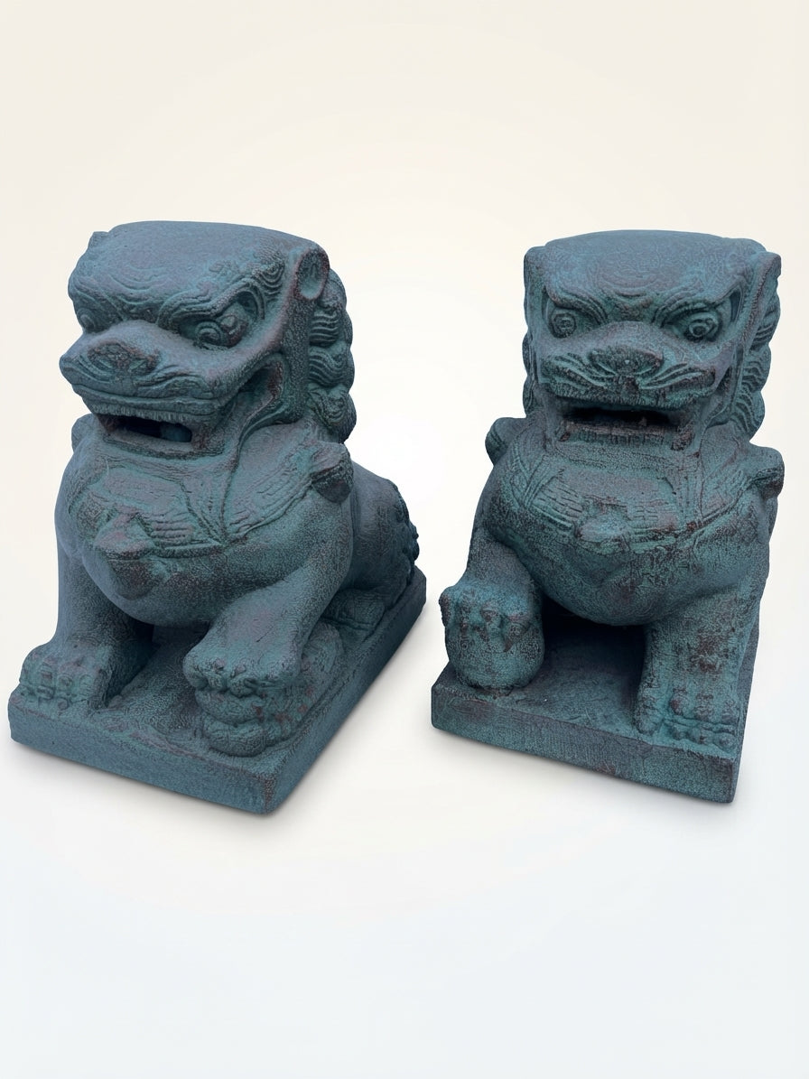 A pair of traditional Chinese stone lion statues with a weathered teal-green patina, displayed side-by-side against a plain off-white background.