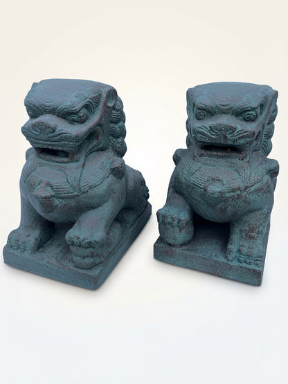 A pair of traditional Chinese stone lion statues with a weathered teal-green patina, displayed side-by-side against a plain off-white background.