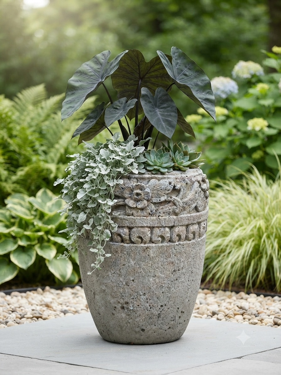 A large round concrete planter with carved floral and scroll details, filled with green foliage and succulents, set on a stone patio in a garden.