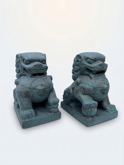 A pair of traditional Chinese stone lion statues with a weathered teal-green patina, displayed side-by-side on a clean white background.