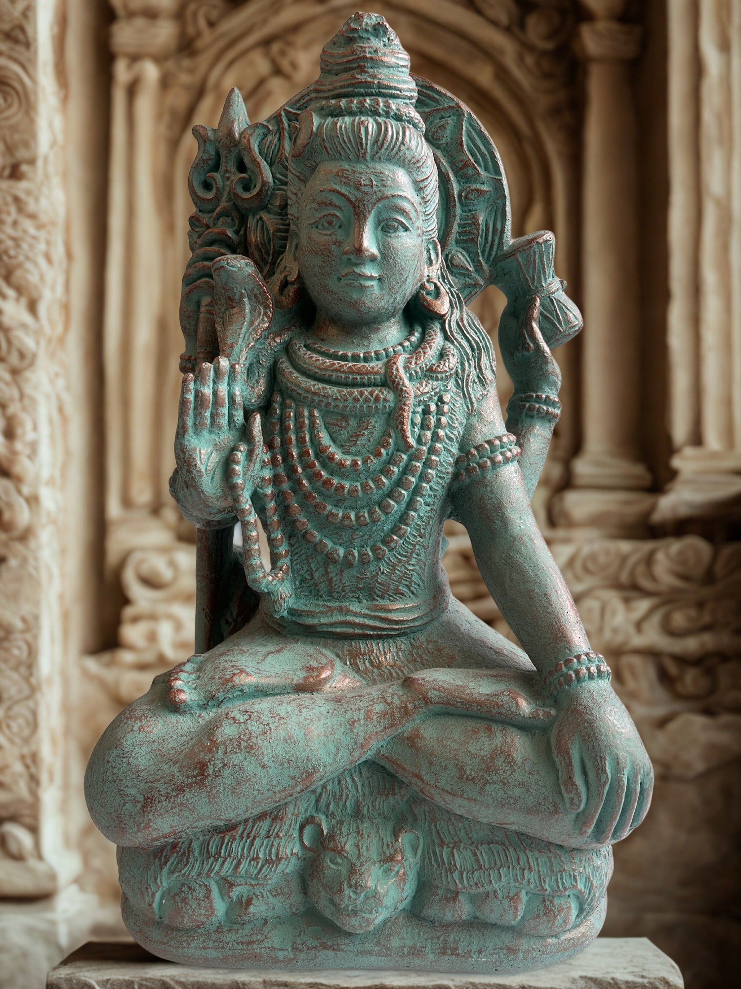 Statue of Hindu diety Shiva in a meditative pose with intricate details against a stone wall