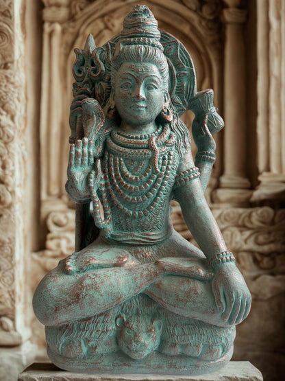 Statue of Hindu diety Shiva in a meditative pose with intricate details against a stone wall