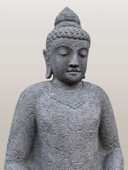 Stone statue of a seated Buddha with intricate carvings on a plain background