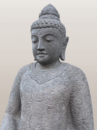 Stone statue of a seated Buddha with intricate patterns on a plain background