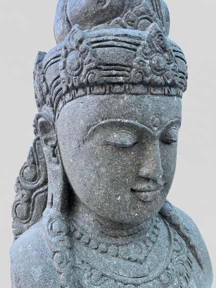 Stone statue of a deity with intricate details on a plain background