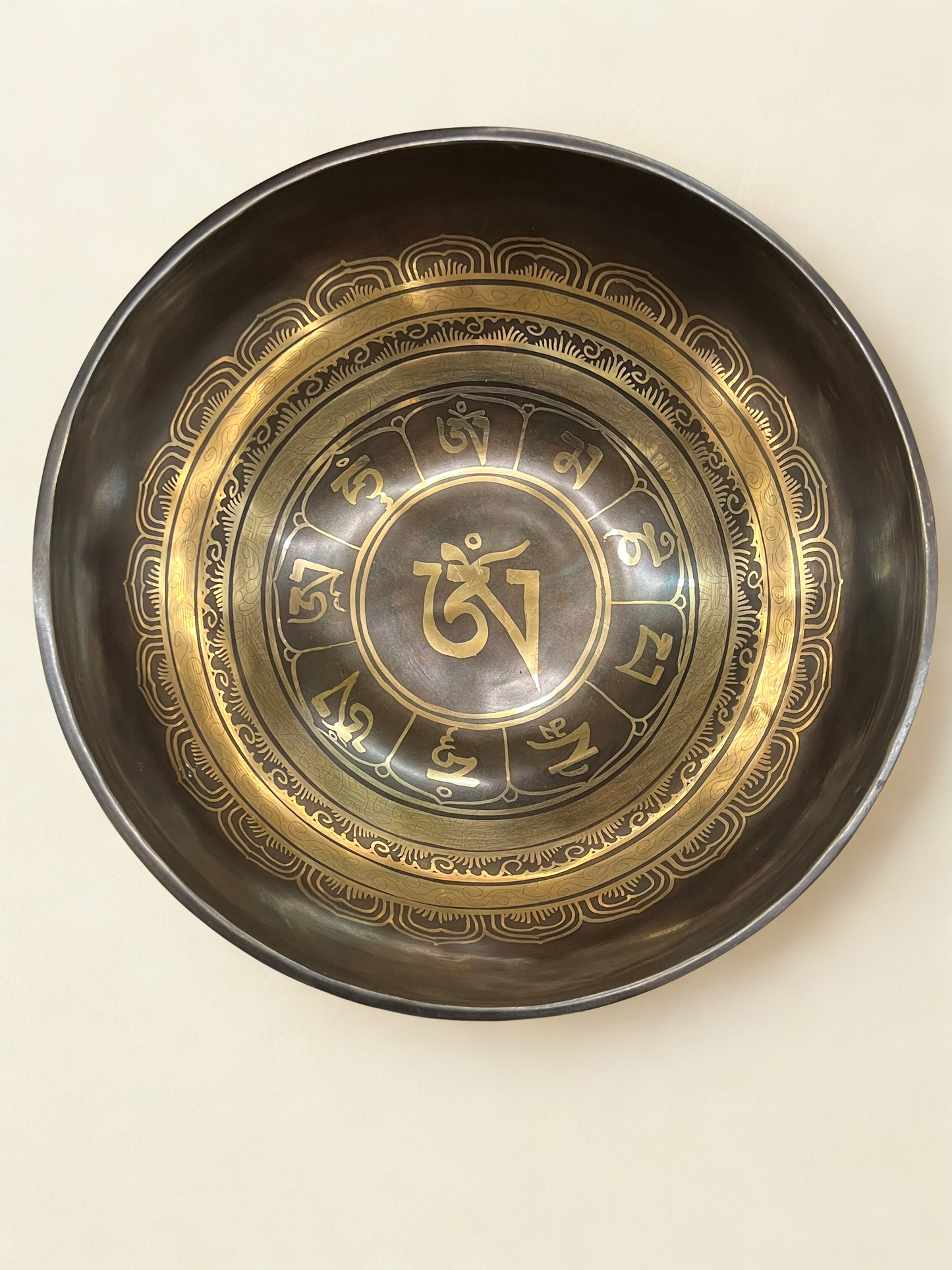 Decorative singing bowl with gold and black design on a beige background