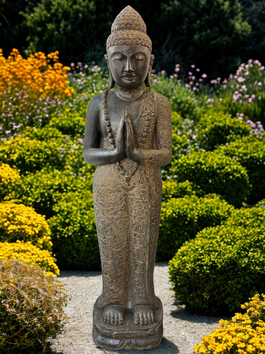 Statue of a standing Buddha figure in a garden with flowers and shrubs