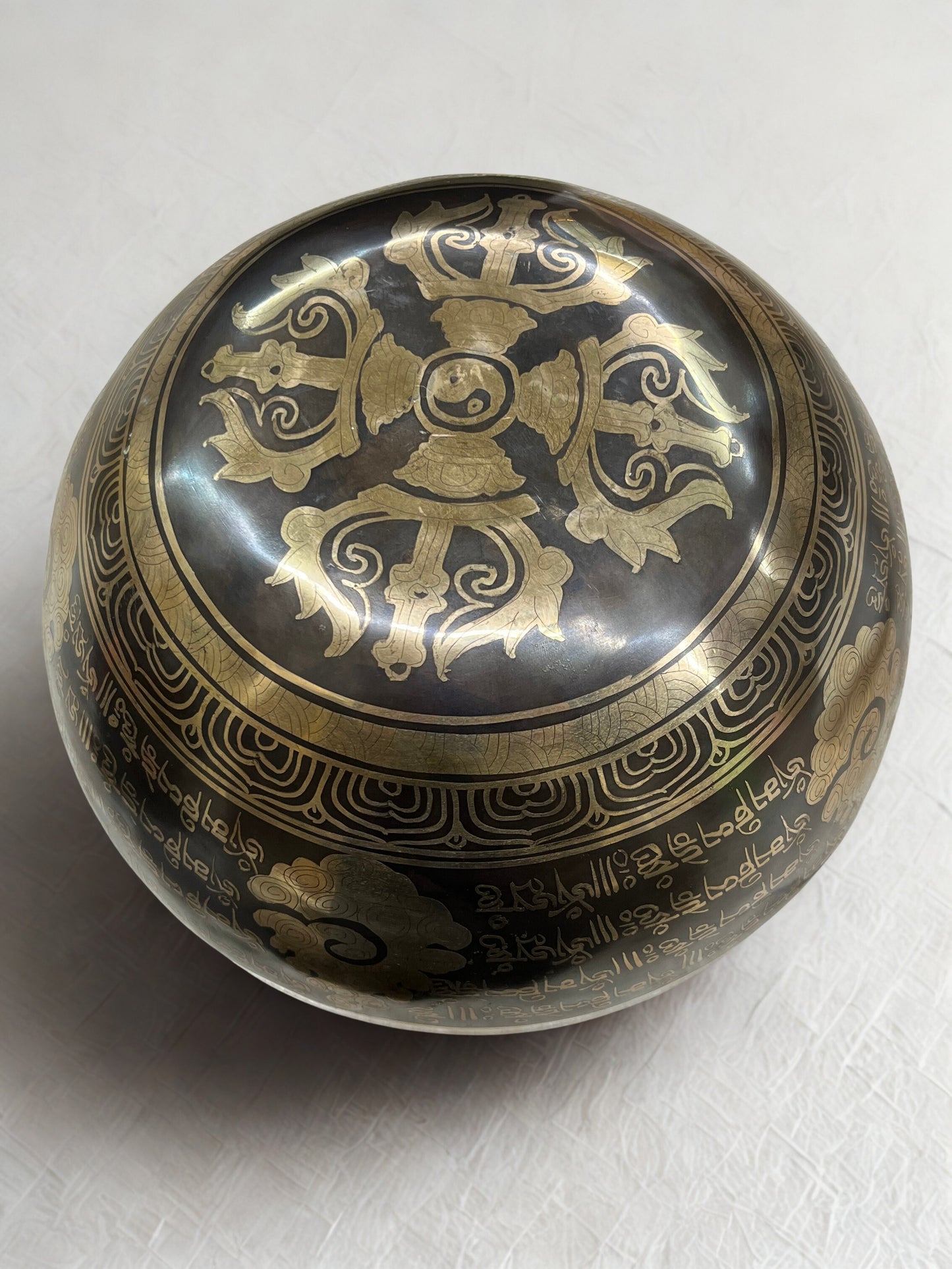 Bottom of a decorative Tibetan singing bowl with intricate gold designs on a white background