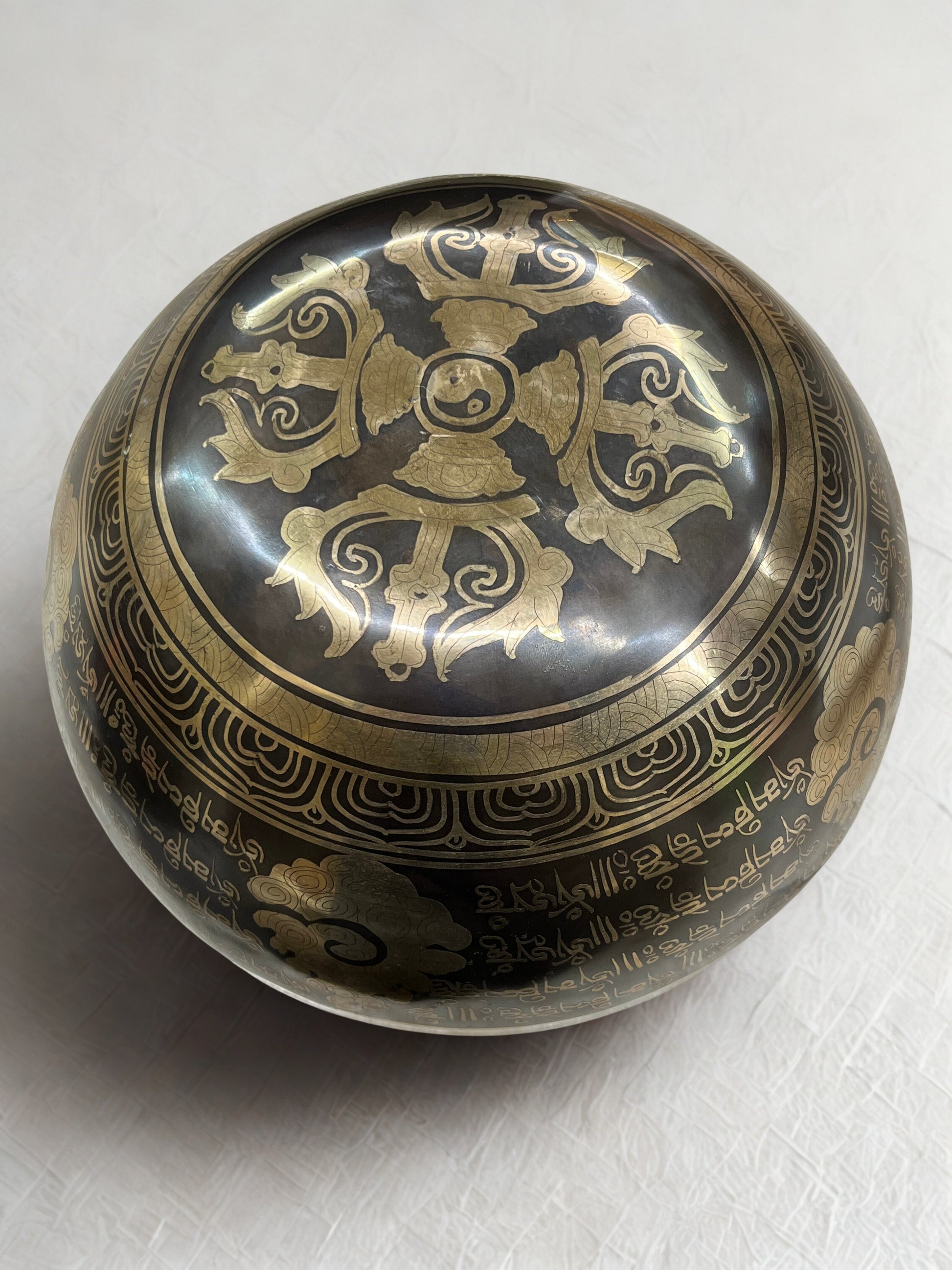 Bottom of a decorative Tibetan singing bowl with intricate gold designs on a white background