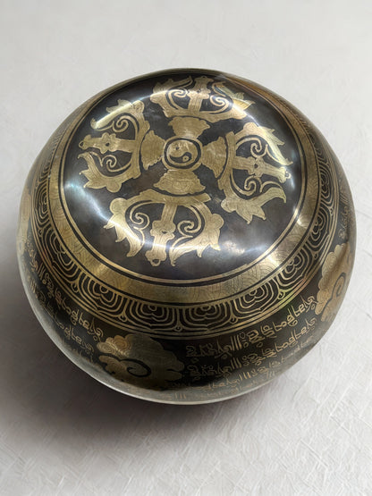 Bottom of a decorative Tibetan singing bowl with intricate gold designs on a white background