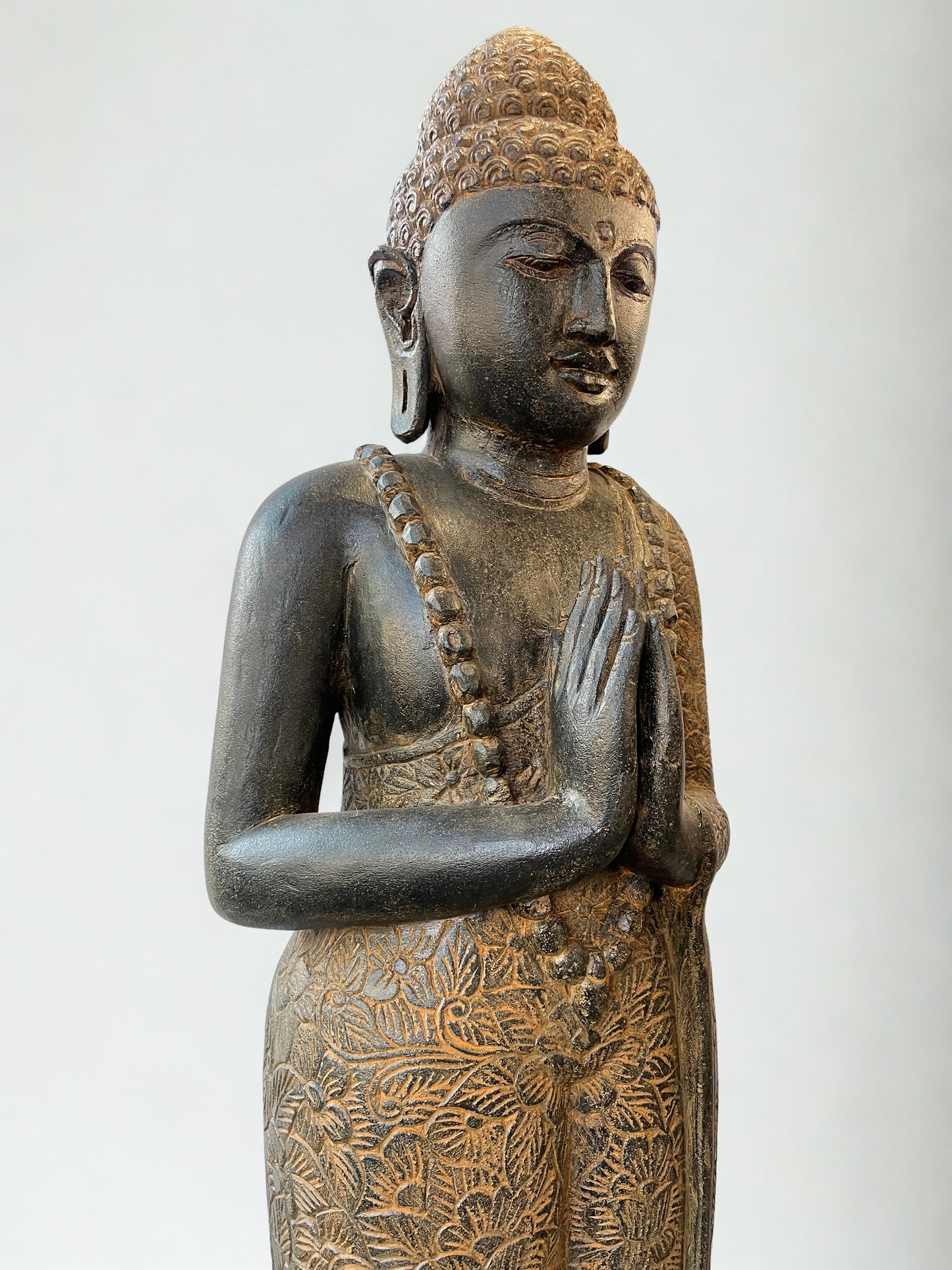 Bronze statue of a standing Buddha with intricate details on a white background