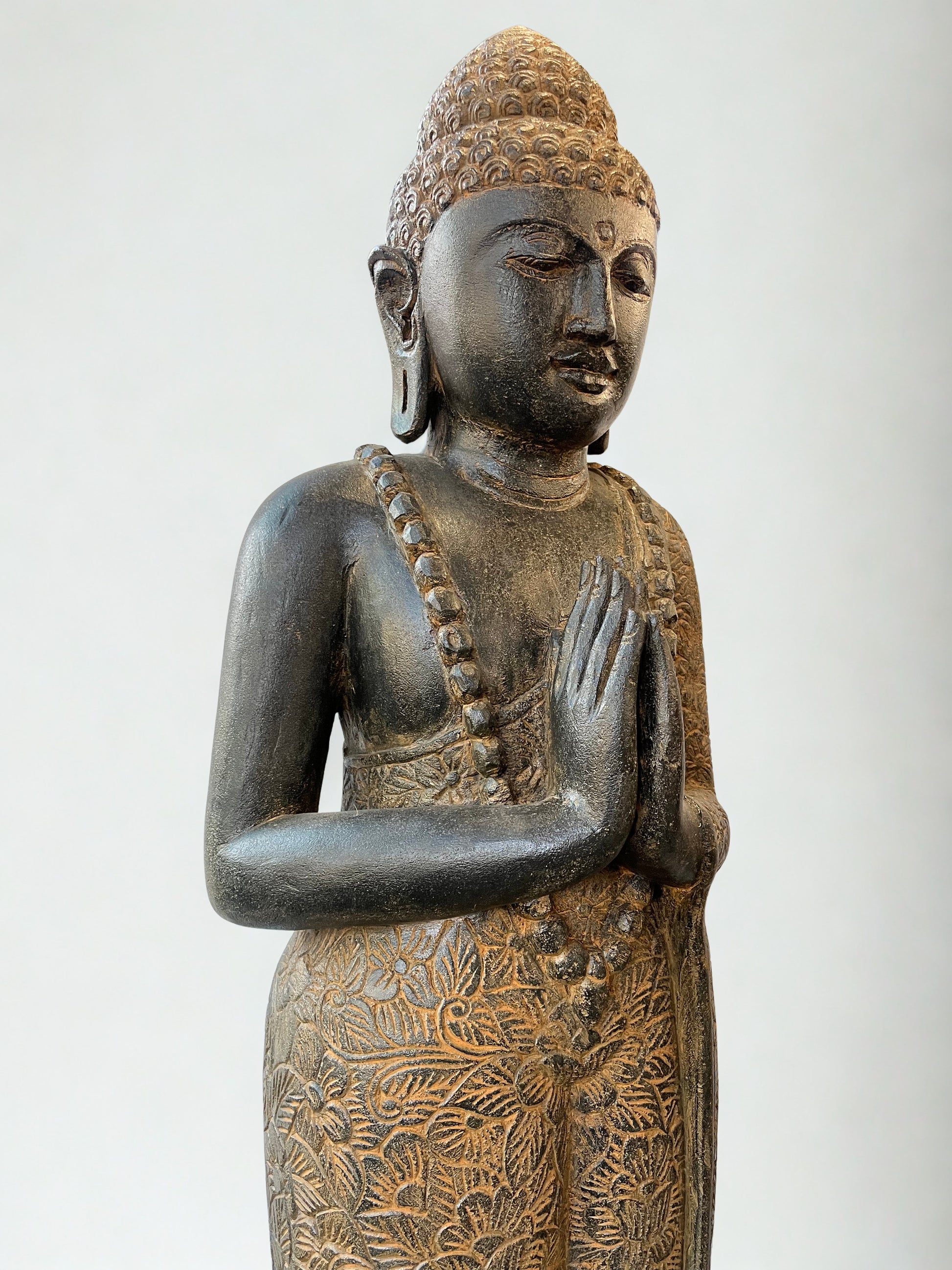 Bronze statue of a standing Buddha with intricate details on a white background