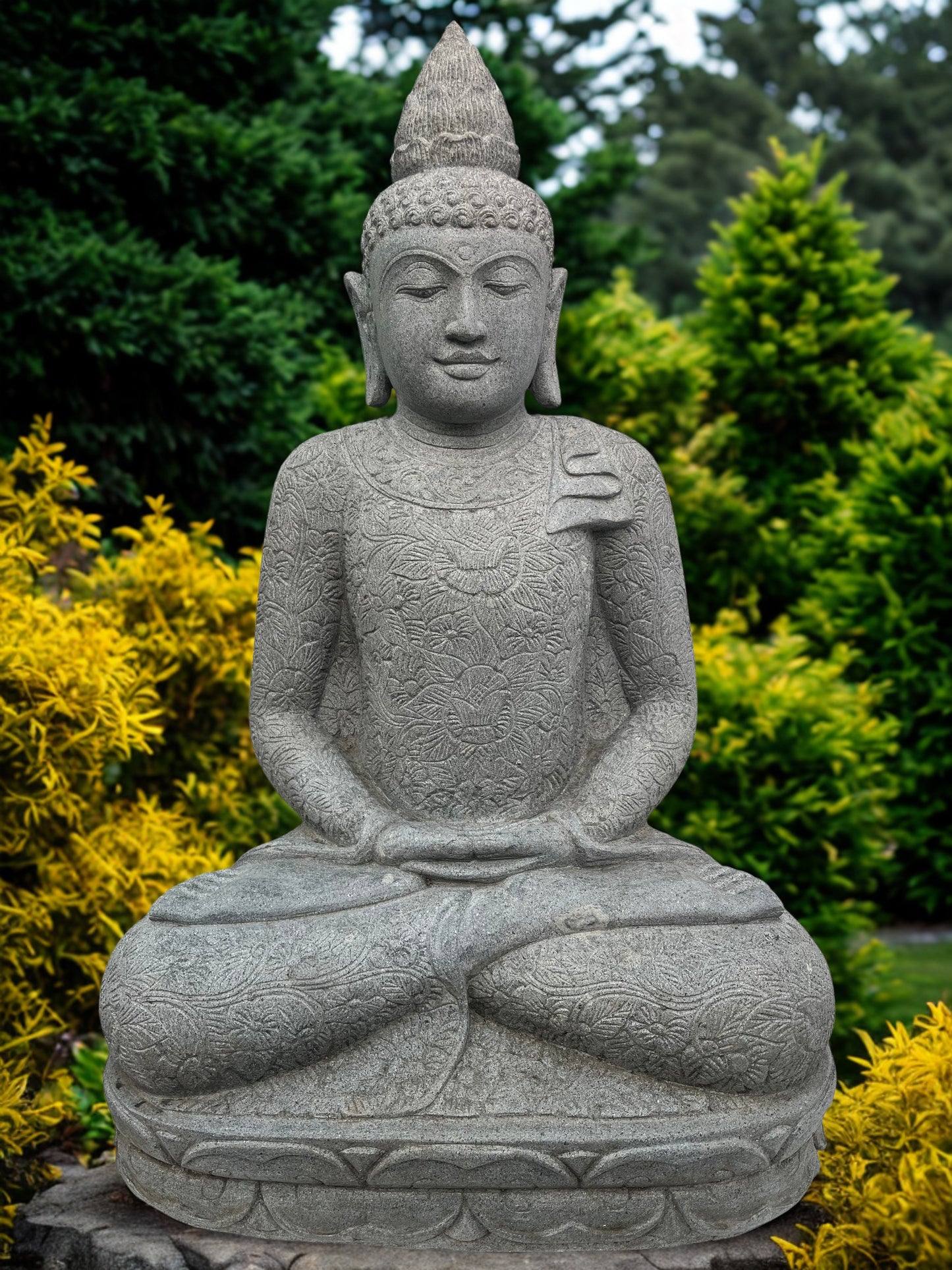 Stone statue of a seated Buddha in a garden setting with green and yellow plants.