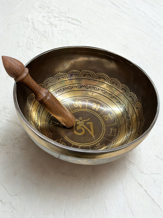 Brass singing bowl with engraved symbols and wooden striker on a light background